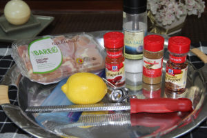 Ingredients to make Moroccan Chicken, including boneless chicken thighs, paprika, ground cumin, crushed red pepper, sea salt and a fresh lemon. All on a round stainless serving tray with silver measuring spoons and a microplaner also on the tray
