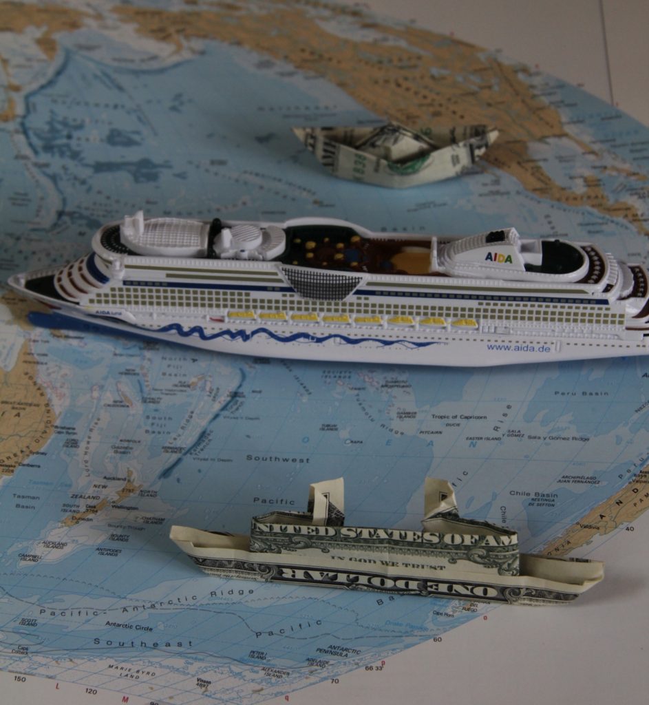 One cruise ship model and two dollar origami boats, on a world map