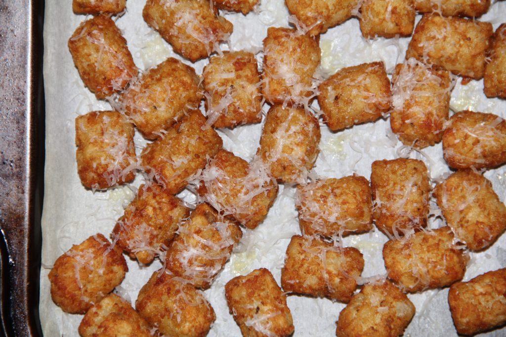 Tater tots, on a cooking pan, sprinkled with fresh parmesan cheese and truffle oil, ready to put on a serving dish.