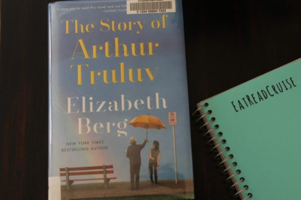 The book The Story of Arthur Truluv by Elizabeth Berg, on a wood table with the EatReadCruise notebook off to the side