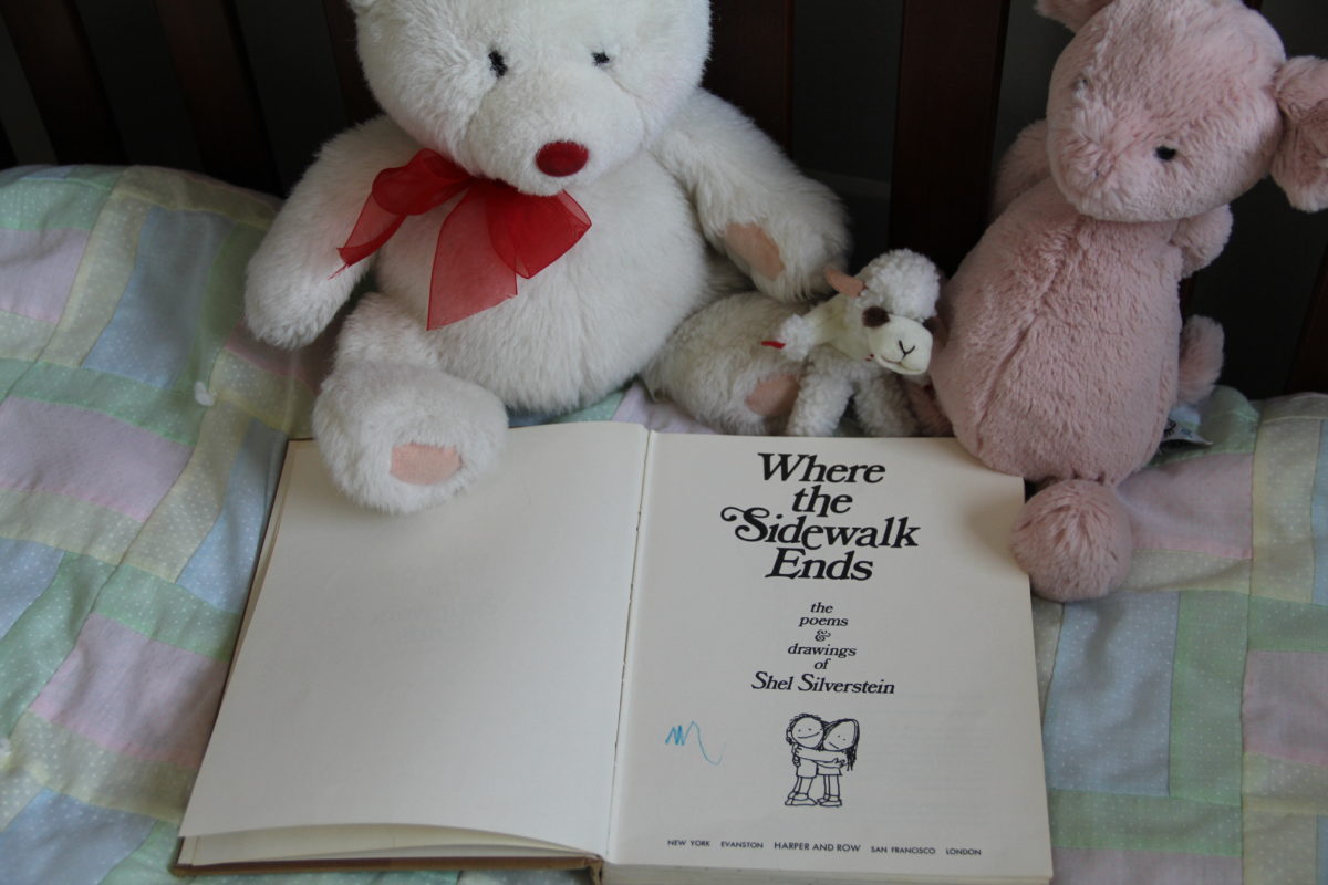 Open book, Where the Sidewalk Ends, in a crib, on a baby quilt, with three stuffed animals surrounding it