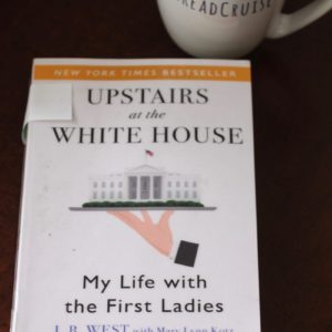 Paperback book, Upstairs at the White House: My Life with the First Ladies, with a cup of tea in a cream colored EatReadCruise mug off to the side