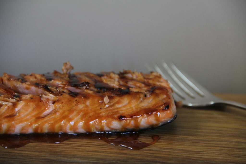Alaskan Style Glazed Salmon, cooked and on a wood cutting board. Close-up with a fork peaking in the upper right hand corner