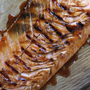 Grilled Alaskan style glazed salmon, on a wood board, drizzled with glaze sauce