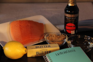 Ingredients for Alaskan style glazed salmon, including brown sugar, butter, fresh lemon, white wine, tamari and fresh salmon, on a jelly roll pan