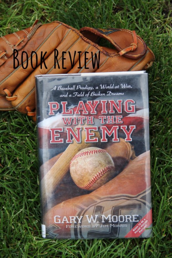 The hardcover book, Playing With the Enemy, lying on green grass, propped up on a leather baseball glove.