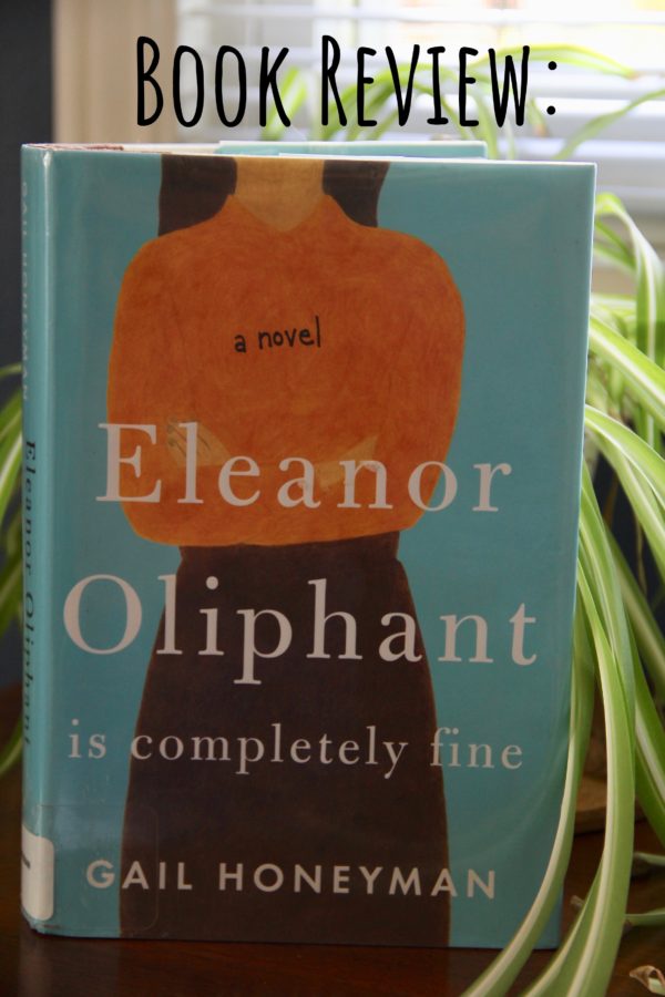 Hardbook copy of Eleanoe Oliphant is ompletely Fine on a wood table, in fromt of window with blinds and a green spider plant on the side of book, book review, book club questions,