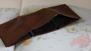 Brown wallet, empty, sitting on a world map, showing 1 of 9 ways to ruin your cruise