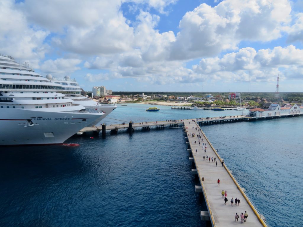 Two cruise ships in a Caribbean cruise port. Thw walkway from the ship to the port is filled with many people. Cruise insurance explained