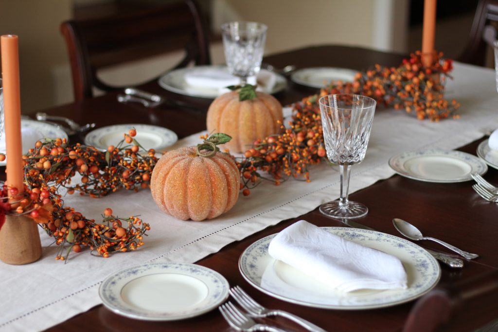 dark wood formal dining room table, set for a fall dinner, with fine china, crystal water goblets, white linen napkins, silver-plated dinner ware with decorative  pumpkins and orange candles in candle holders. What to serve for Thanksgiving.