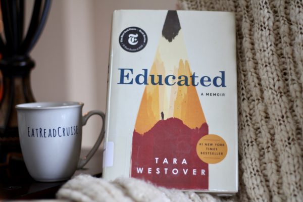 Hardcover edition of the book Educated, by Tara Westover, in front of a cozy cream knitted blanket with a cup of tea next to it