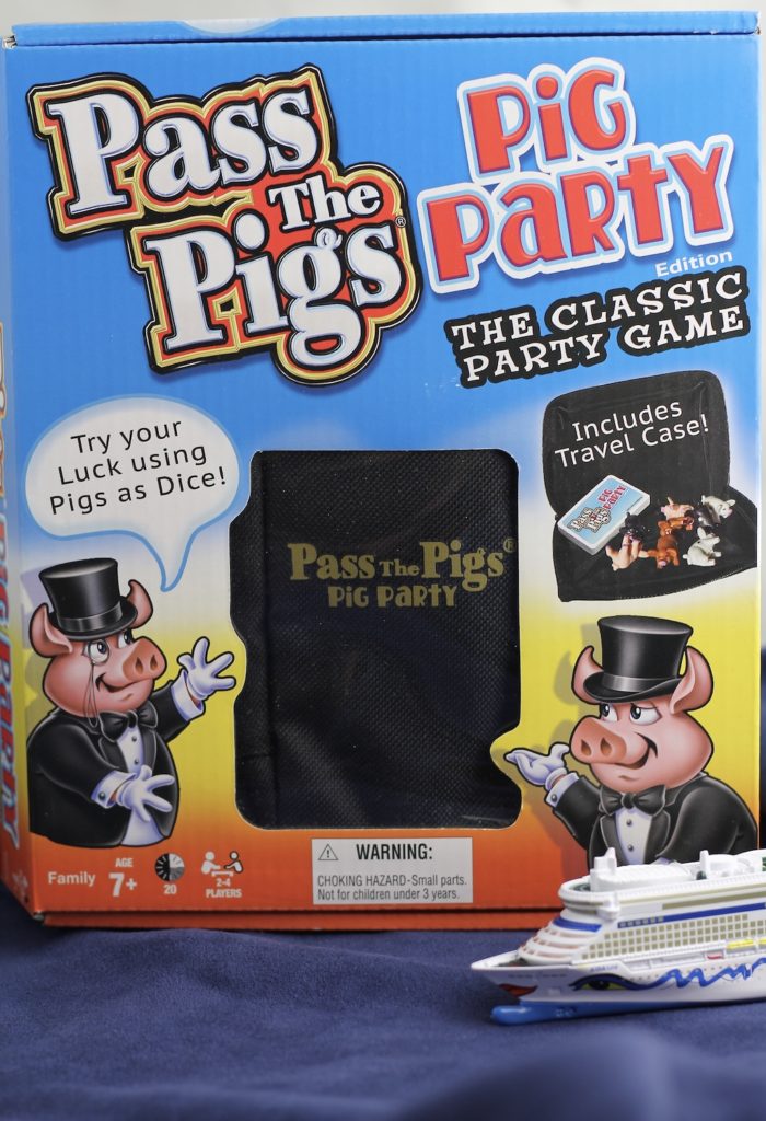 Pass the Piggs dice game, party edition, in box with a small model cruise ship in front of game