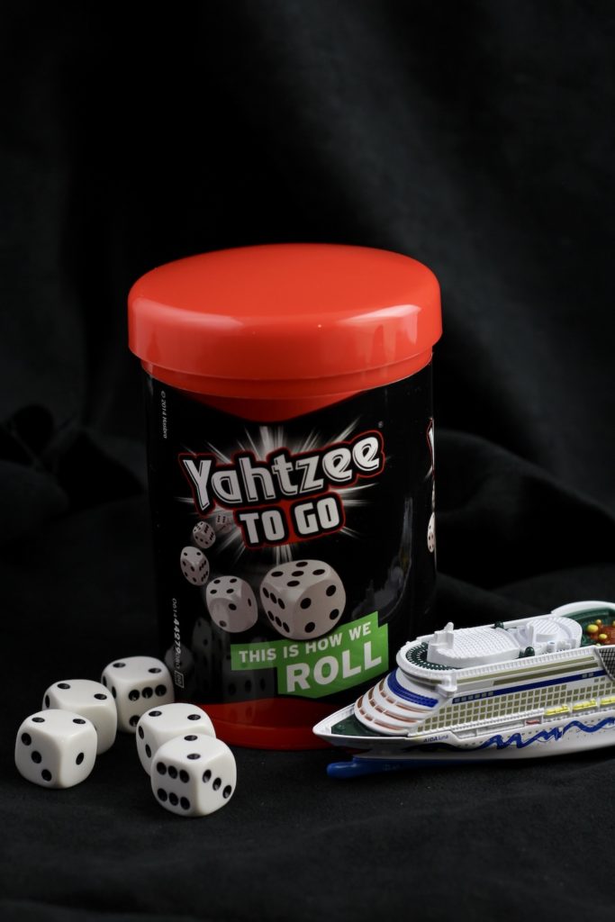 Yathzee travel game, in a red and black plastic cup, showing 5 dice on lower left and a small model of a cruise ship in the lower right