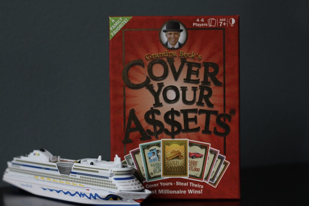 Card game Cover Your Assets, standing on a counter with a model cruise ship on the lower right side of counter
