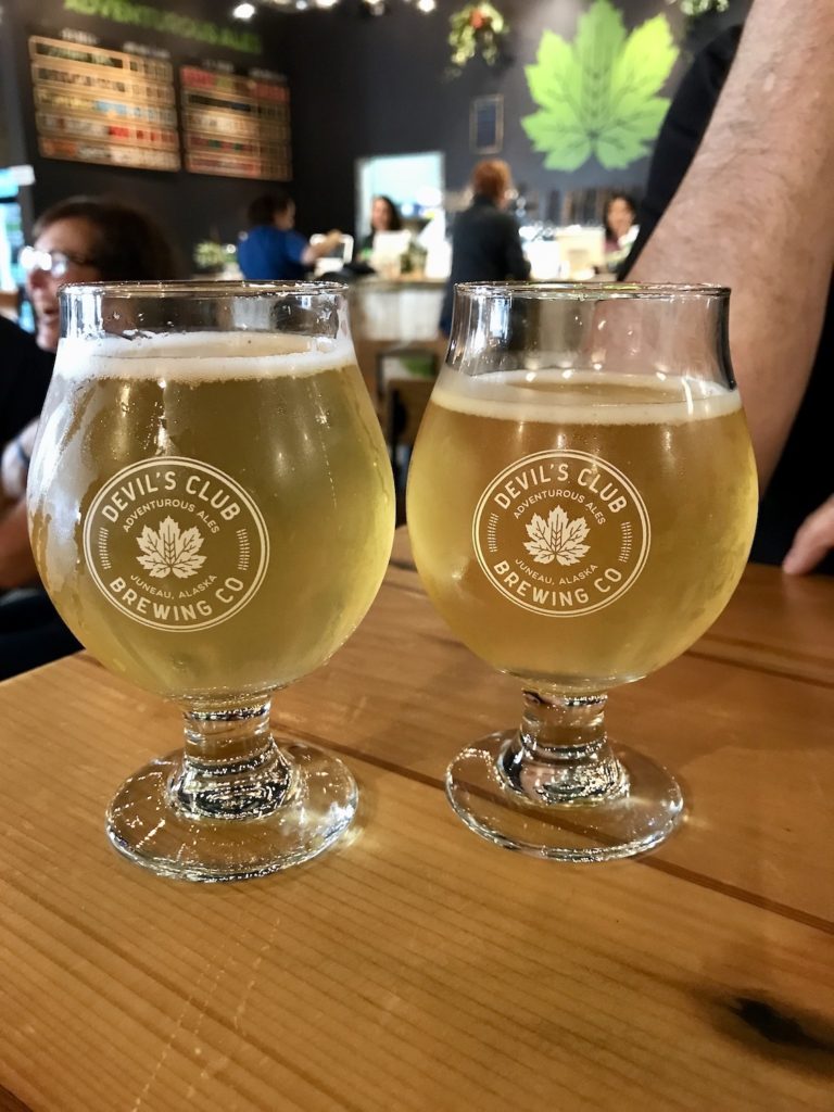 2 glasses of a pilsner beer from Devil's Club brewery on a light wood tabletop. Alaska cruise tips.