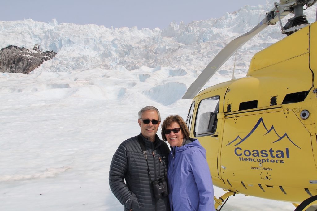 My husband and I standing in front of a yellow helicopter while on the Mendenhall Glacier