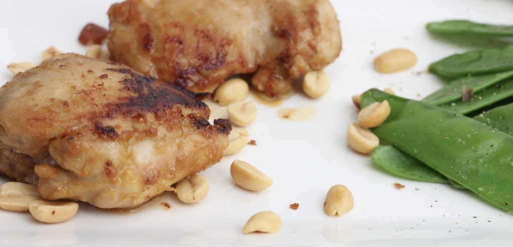 Chicken with peanut sauce on a diner plate ready to eat, along with green pea pods